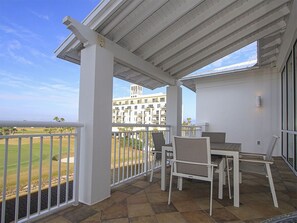 A covered patio with a table and chairs, overlooking a golf course and a building complex.