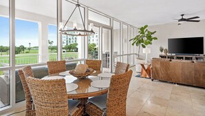 Un vaste espace de vie doté d’une grande fenêtre, d’une table à manger avec des chaises en osier, d’un canapé et d’un téléviseur à écran plat.