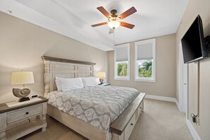 Ein Schlafzimmer mit Bett, Nachttischen, Deckenventilator, Fernseher und Fenstern.