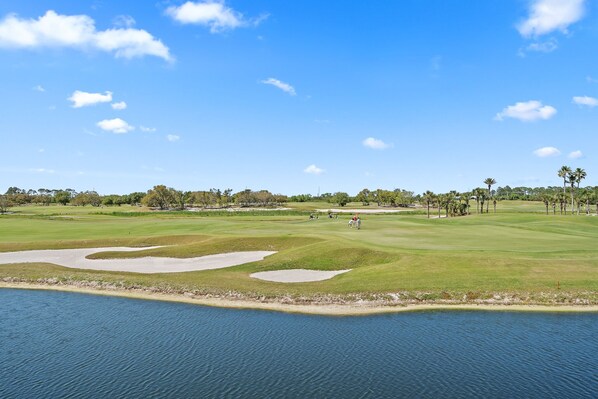 Un campo de golf con una masa de agua al frente y un cielo despejado.