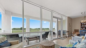 Varanda ampla com vista para um campo de golfe, mobiliada com um sofá, cadeiras e uma mesa redonda.