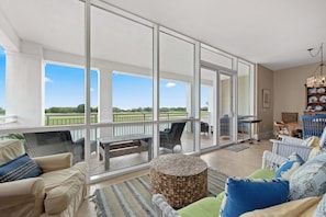 A spacious balcony with a view of a golf course, furnished with a sofa, chairs, and a round table.