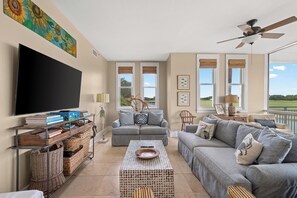 Ein Wohnzimmer mit Flachbildfernseher, zwei Sofas, einem Couchtisch, Korbwannen und einem Deckenventilator.