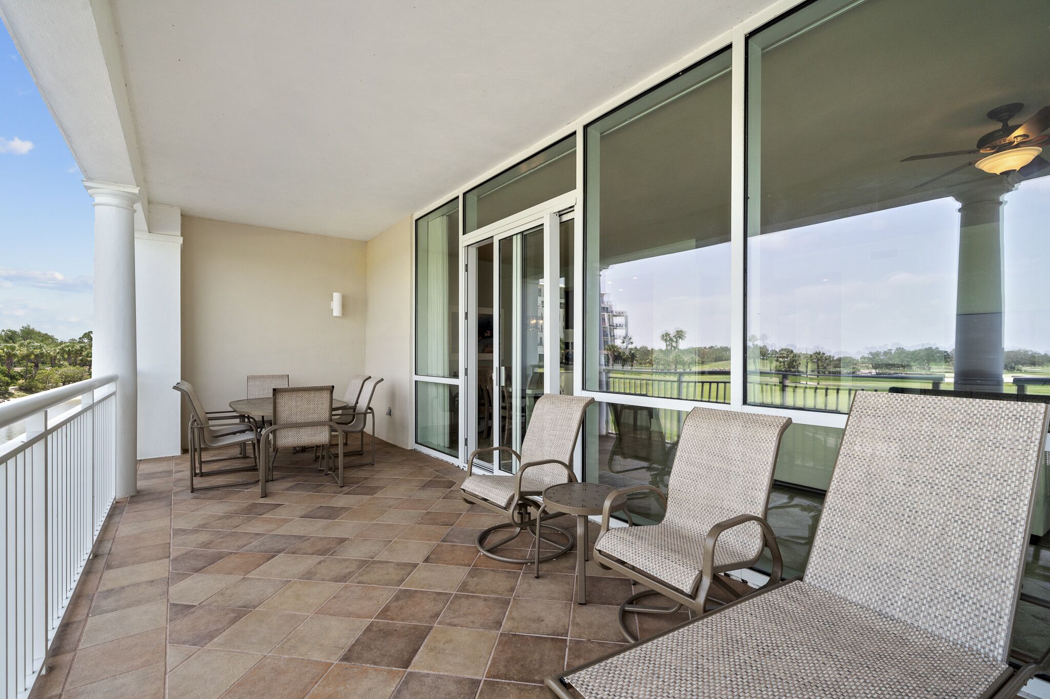 Un balcón con mesa y sillas, ventanas amplias y vista a un campo de golf.