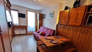 Ein gemütliches Zimmer mit Holztisch, gedecktem Esstisch, einer Couch und einer Küchenzeile.