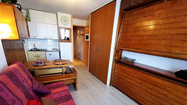 Ein kompakter Wohnraum mit Küchenzeile, Essbereich und einem Holzschrank.