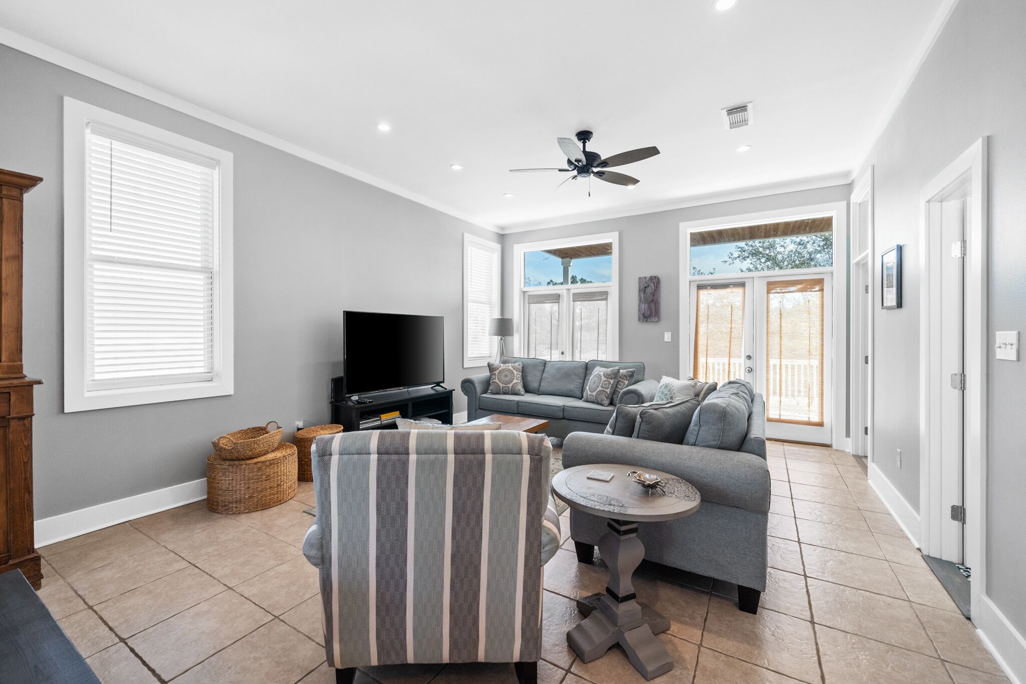 A spacious living room with a gray sofa, a television, and a ceiling fan.