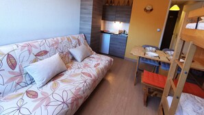 A compact living space with a sofa, a bunk bed, a small kitchen area, and a dining table.
