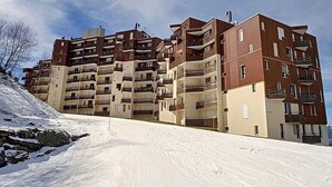 A multi-story residential building with balconies, situated on a snow-covered slope.