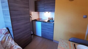 A compact kitchen with a built-in stove, a small sink, and a microwave. There is a wooden cabinet and a wall-mounted clock.