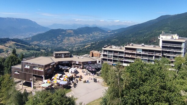 A hotel with multiple floors, outdoor seating area with umbrellas, and a view of surrounding mountains.