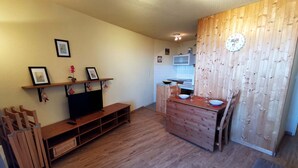 A compact living space with a wooden bench, a TV, and a small kitchen area with a microwave. - 2-Room Cabin at the Foot of the Slopes - 4 Bunk Beds, Pets Allowed (Les Adrets-Prapoutel)