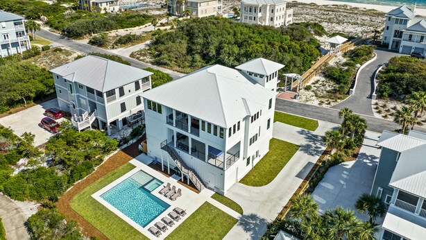 A modern beachfront property with a large pool, multiple buildings, and a view of the ocean.