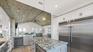 A modern kitchen with a large island, stainless steel appliances, and a rustic ceiling.