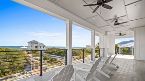 A covered outdoor area with white Adirondack chairs, a view of the ocean, and a mountain in the distance.