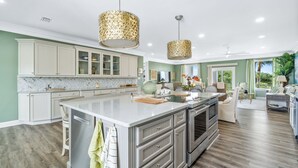 A spacious kitchen with a large island, white cabinetry, and a marble backsplash.