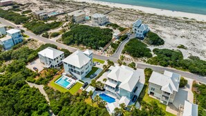 An aerial view of a coastal residential area with multiple houses, a beach, and a clear view of the ocean.