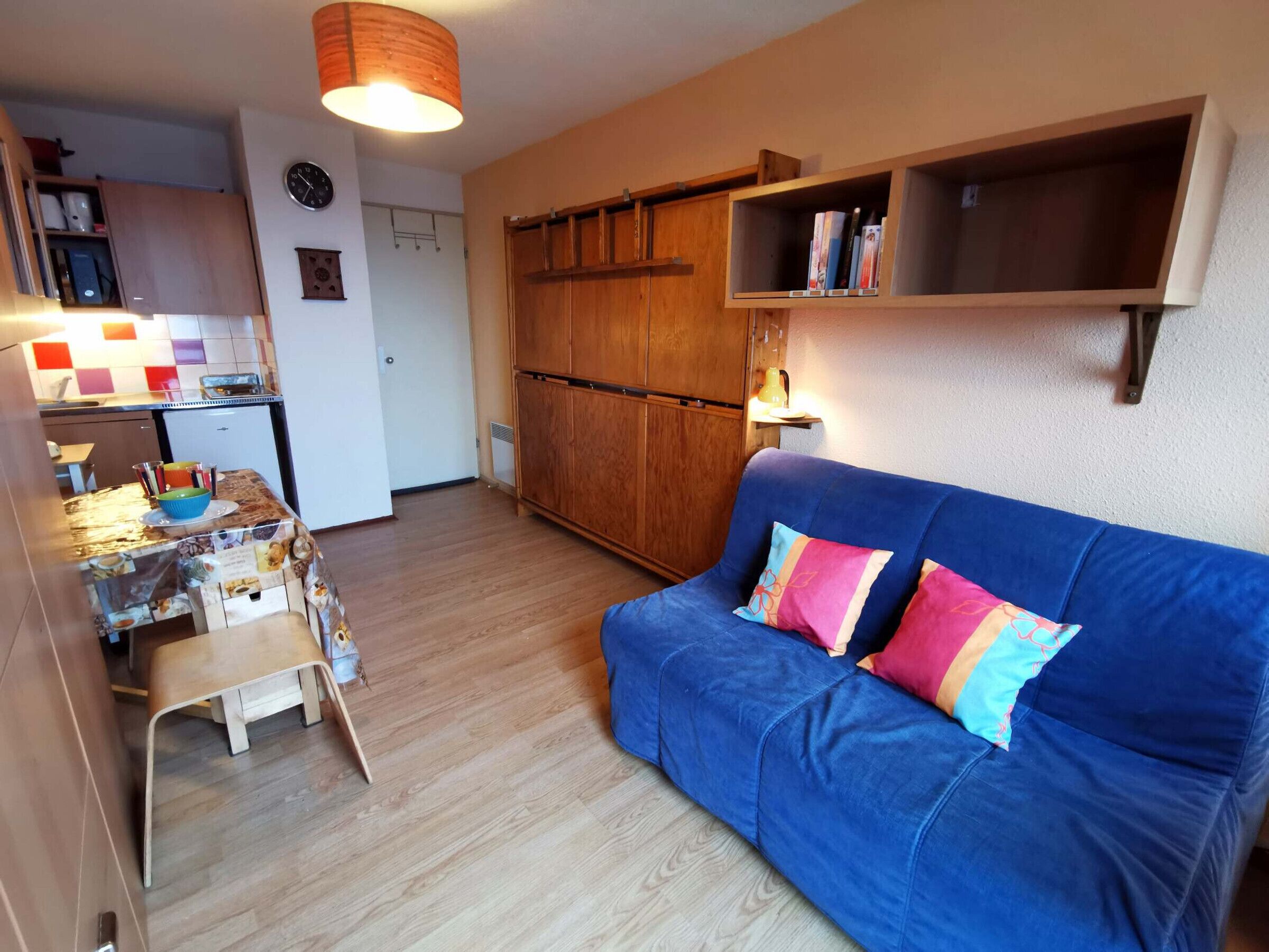 Un espace de vie compact comprenant un canapé bleu, des meubles en bois, un coin cuisine et un espace repas.
