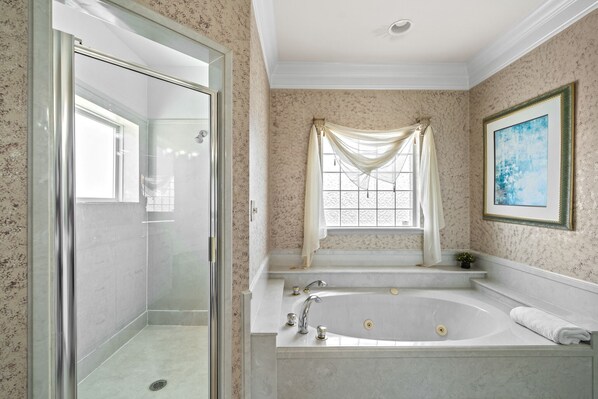 Un baño con ducha de mampara, bañera independiente y ventana con cortinas.