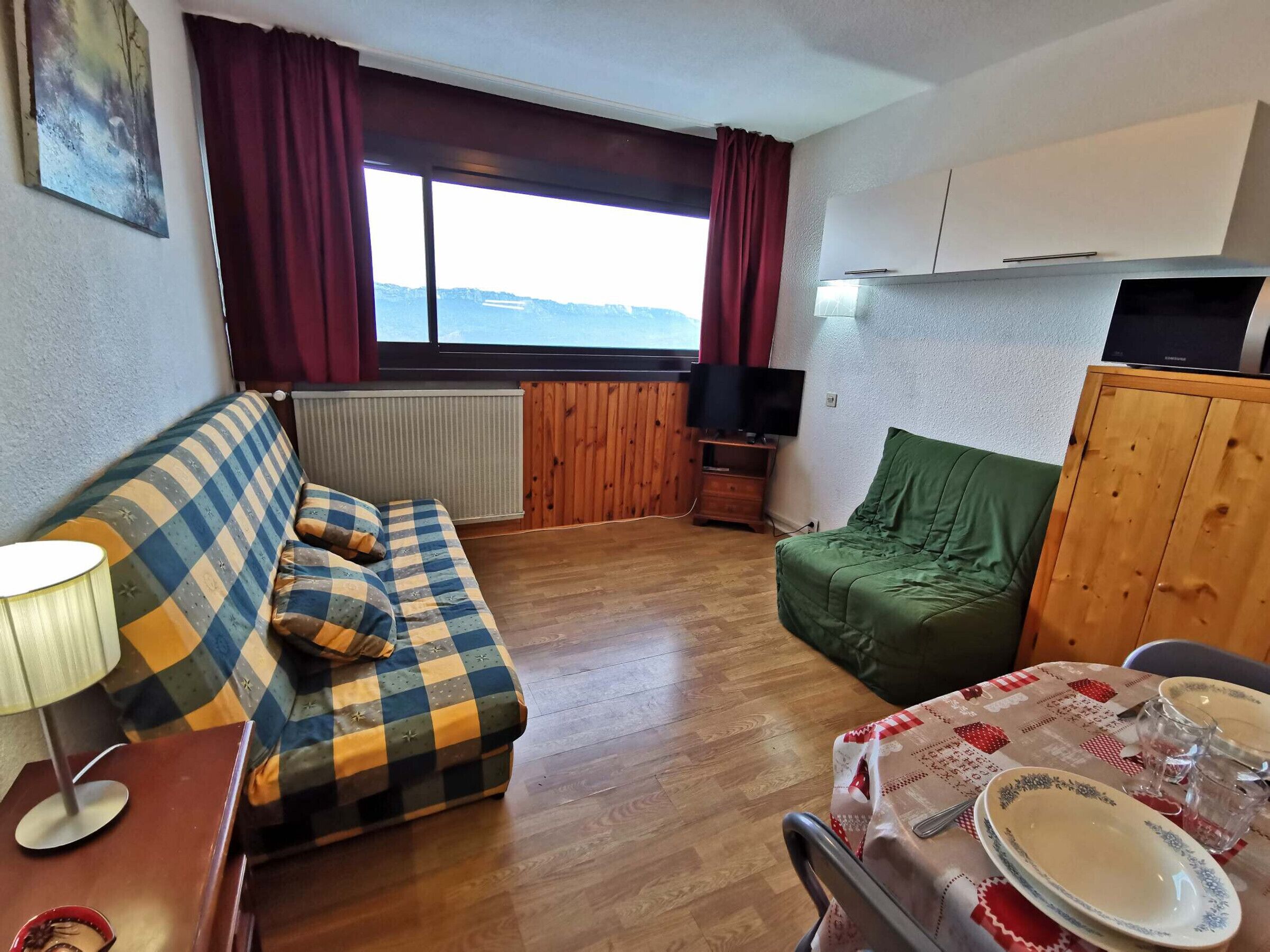 A cozy living room with a sofa, a small table with plates and glasses, a television, and a view of the outdoors.