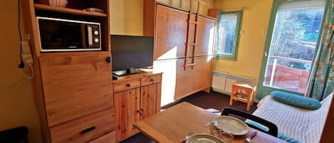 Una cocina compacta con armarios de madera, un microondas integrado y un televisor.