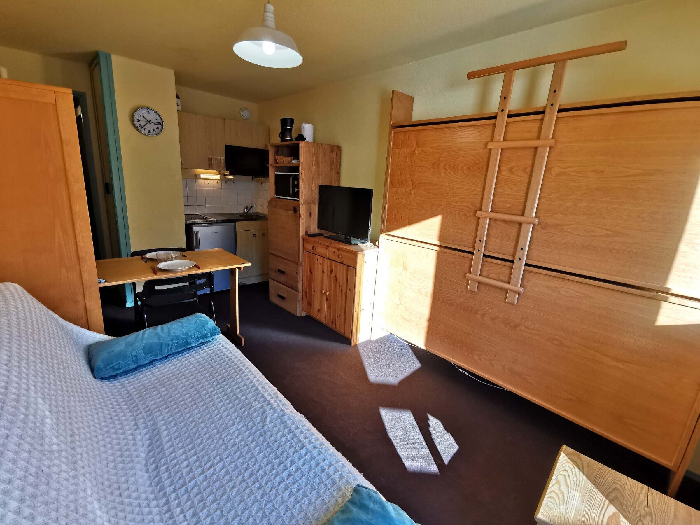 A compact room with a bed, kitchenette, and a TV.