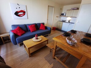 A living room with a blue sofa, red cushions, a wooden coffee table, and a dining table with plates and glasses. - Cozy 2-room apartment, ski-in/ski-out, 2-6 pax, Les Adrets-Prapoutel (Les Adrets-Prapoutel)