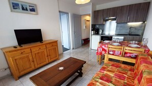 A living room with a wooden TV stand, a coffee table, and a sofa. There is a kitchen area with a dining table set for four.