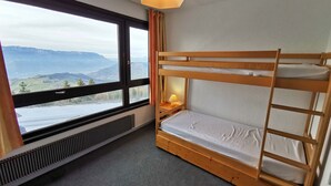 A bunk bed room with a view of mountains through a large window, a heater, and a bedside lamp.
