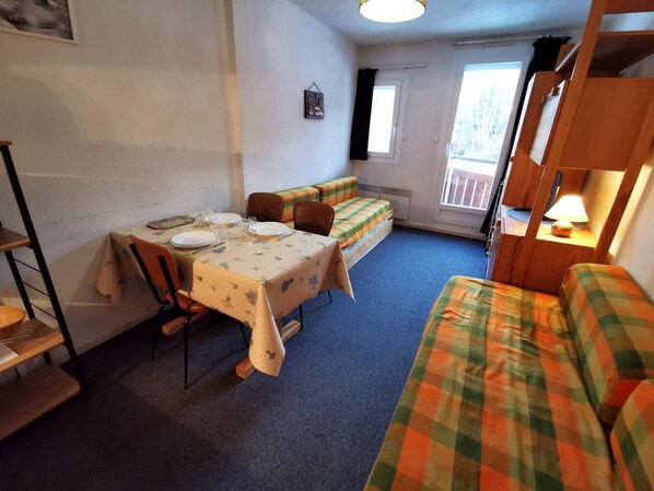 Une pièce chaleureuse avec une table à manger dressée pour deux personnes, un banc et un lit superposé équipé d’une lampe.