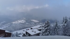 A snow-covered mountain landscape with a view of a chalet-style building with multiple rooms and a car parked in front.