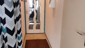 A narrow hallway with a patterned curtain on the left, a brown mat at the entrance, and a door with a mirror reflection. - Renovated studio near center, balcony and TV (Les Adrets-Prapoutel)