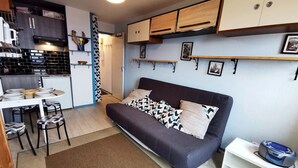 A compact living space with a kitchenette, a sofa with patterned cushions, and a small dining table. - Renovated studio near center, balcony and TV (Les Adrets-Prapoutel)