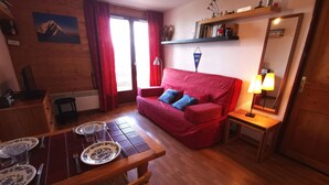 A cozy living room with a red sofa, a wooden dining table with plates, and a mirror on the wall. - Apartment in Adrets-Prapoutel, 2 rooms, balcony, close to slopes and shops (Les Adrets-Prapoutel)