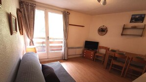 A living room with a sofa, a television, a dining table with chairs, and a sliding glass door. - 2-room apartment in Adrets, ski-in/ski-out, pets allowed (Les Adrets-Prapoutel)