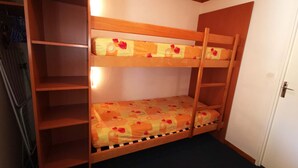 A bunk bed with a wooden frame, a lower bunk with a floral-patterned mattress, and a top bunk with a plain mattress. There is a white door to the right and a metal rack to the left. - 2-room at the foot of the slopes, near lifts (Les Adrets-Prapoutel)