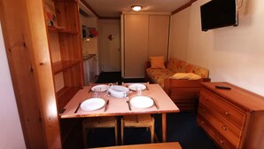 A compact room with a wooden dining table set for four, a sofa, a dresser, and a TV mounted on the wall. - 2-room at the foot of the slopes, near lifts (Les Adrets-Prapoutel)