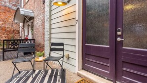 Une terrasse avec deux chaises et une table, une porte violette et un mur en briques.