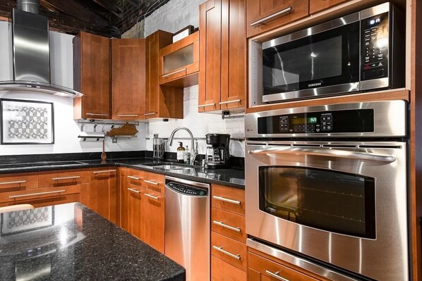 A modern kitchen with stainless steel appliances, wooden cabinets, and a granite countertop.