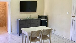 Et lille værelse med et hvidt bord, to stole, et fladskærms-tv på væggen, en mikrobølgeovn og et lille skab.