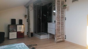 Ein Schlafzimmer mit einer Schiebetür zu einem Duschbereich, einem Bett mit gemustertem Bettbezug und einer kleinen weißen Kommode.