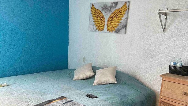A bedroom with a bed, pillows, a dresser, a wall art piece, and a remote control on the bed. - Casa Vazquez Anexo 1 (Pachuca)