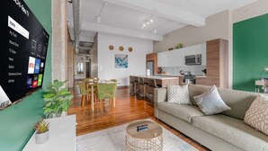 A modern living room with a sofa, coffee table, and a TV mounted on the wall displaying streaming services. - 3BR Downtown Dallas Loft | Fan Fest + Valet + Pool (Dallas)