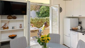 Una cocina moderna con armarios blancos, televisor integrado y un comedor con mesa y sillas de vidrio.