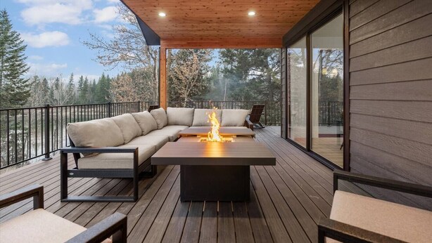Eine überdachte Terrasse im Freien mit Holzboden, einem integrierten Feuerbereich und einer gepolsterten Sitzecke.