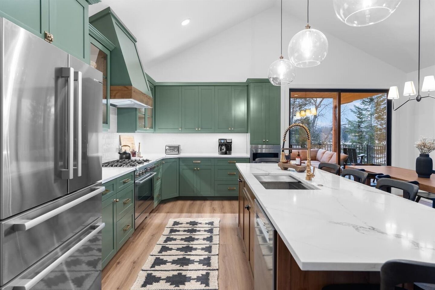 A modern kitchen with green cabinets, stainless steel appliances, and a large island with a sink.
