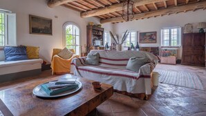A rustic room with a wooden ceiling, a sofa, a table with books, and a window.