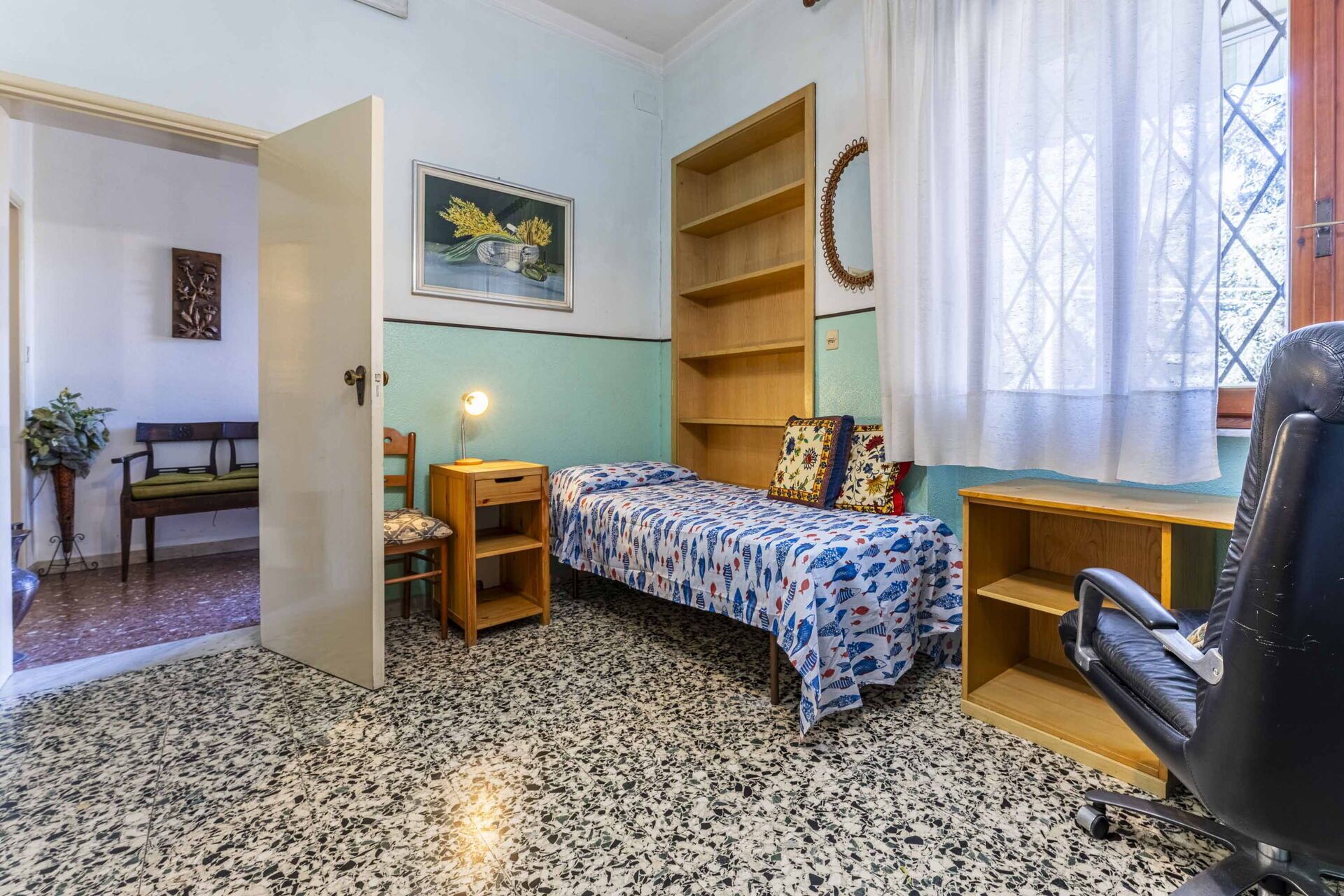 Ein kleines Zimmer mit einem Bett, einem Schreibtisch, einem Stuhl, einem kleinen Tisch, einem Regal und einem Fenster mit Vorhängen.