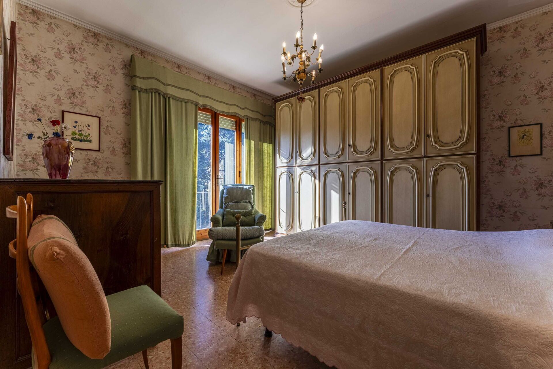Ein Schlafzimmer mit einem großen Bett, einem Holzstuhl, einem grünen Sessel, einem Schminktisch und einem Kleiderschrank.