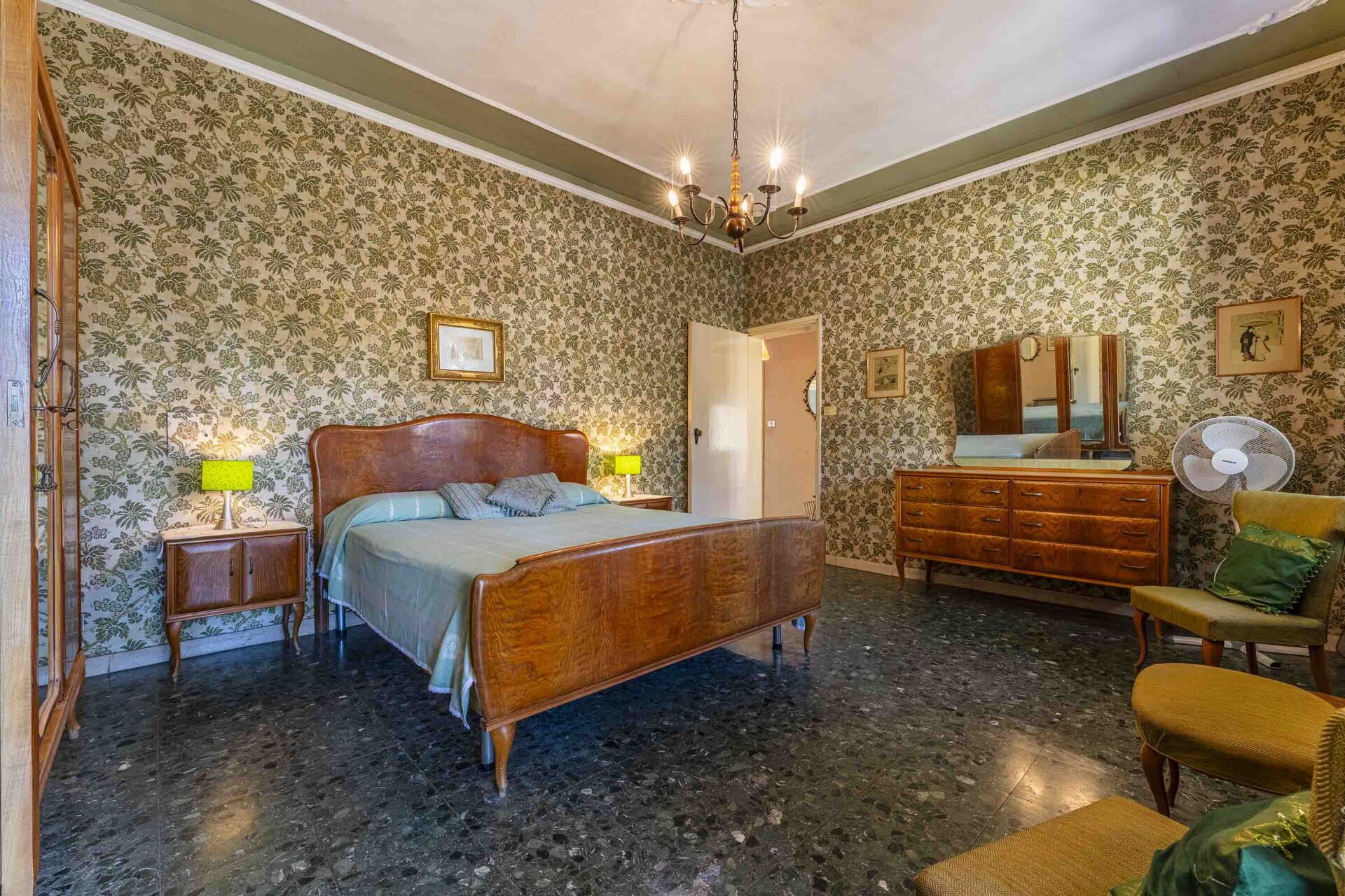 A bedroom with a wooden bed, a dresser, a mirror, and a fan.